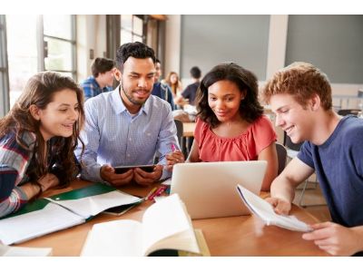 A male volunteer works with three Junior Achievement students using technology.